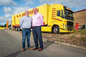 W.S. Dennison Managing Director, William Dennison, with long term Transport Manager, Liam Taggart, standing in front of one of the company's yellow and red anniversary truck and trailers